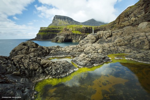 The picturesque village of Gasadalur which is overlooked by the 612m Heinanova mountain, with a waterfall cascading over a cliff into the Atlantic Ocean.