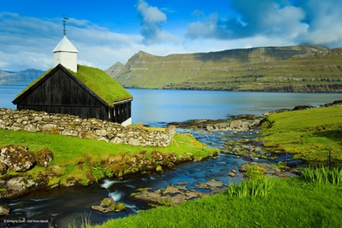A stream running into the Funningsfjordur and a traditional turf or grass roofed church, located in the picturesque village of Funningur.